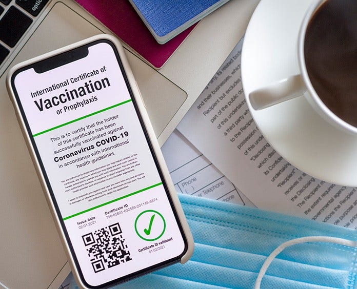 Cell phone screen showing certificate of vaccination cup of coffee and blue mask in background