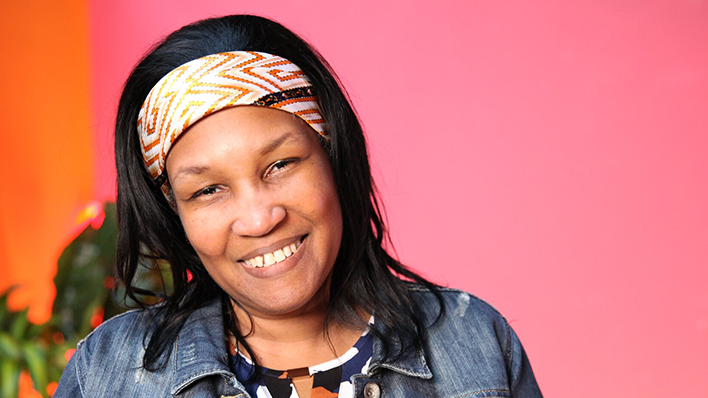 Smiling woman wearing a patterned headband and denim jacket with a colorful background