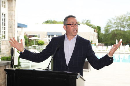 Business professional giving a speech outdoors at a podium with a poolside backdrop