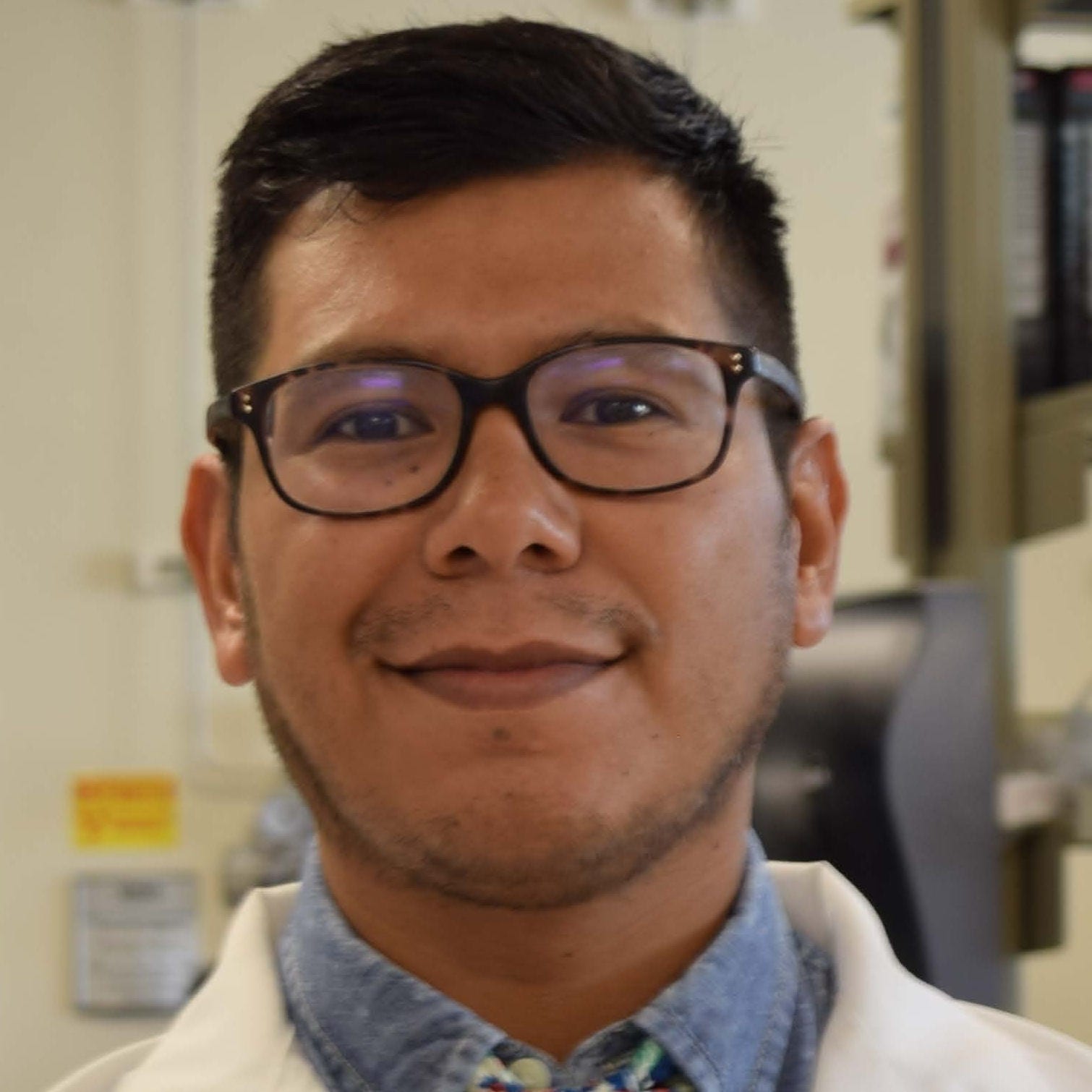 man in dark glasses short haircut in labcoat over denim shirt and colorful tie