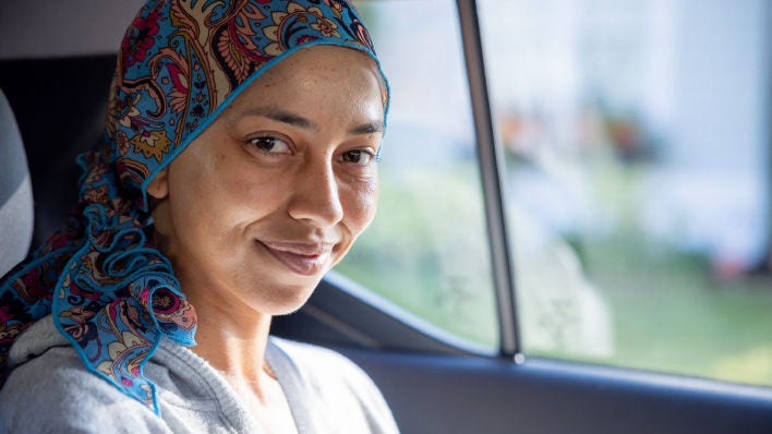 Mujer sonriente con un pañuelo colorido en la cabeza, sentada en un auto