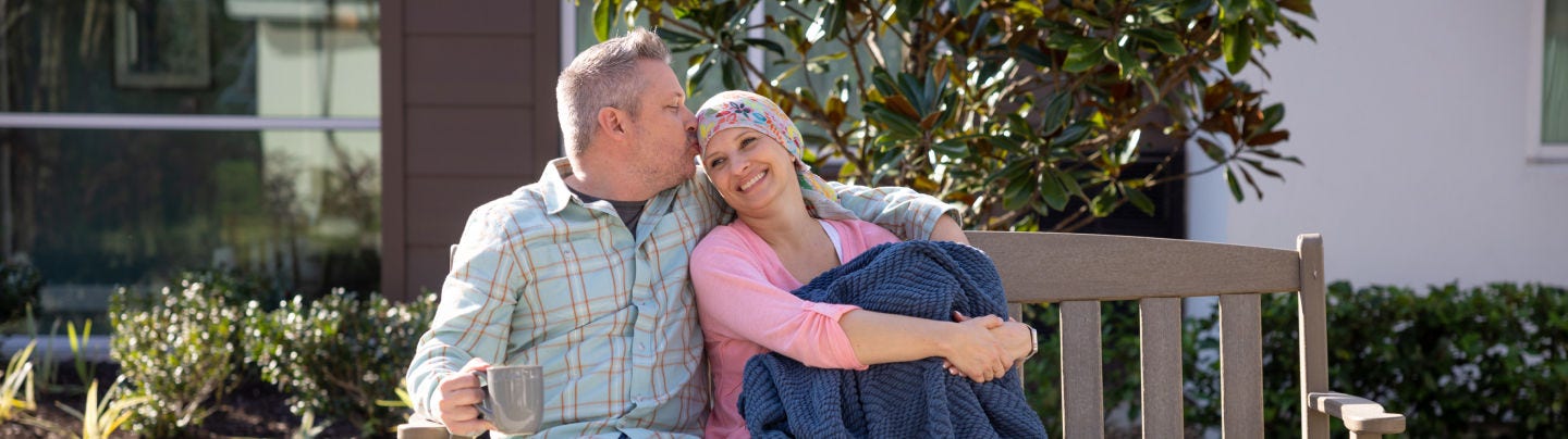 Man comforting a smiling woman wearing a headscarf on a bench outdoors