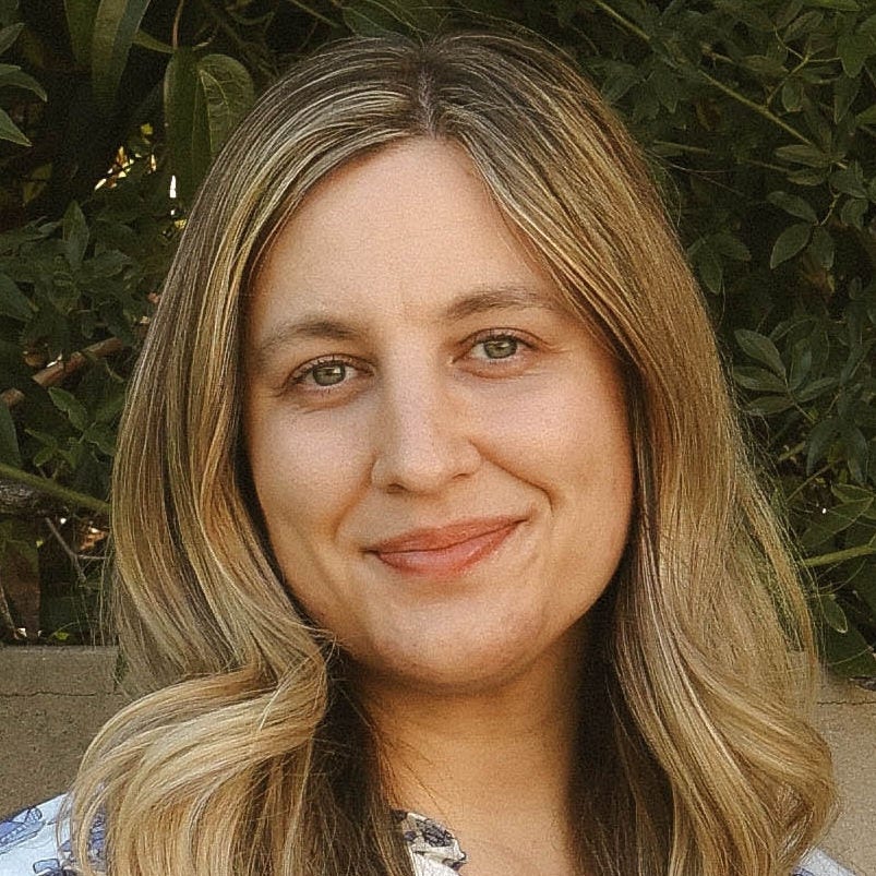 white young woman with long blonde hair in blue and white dress in front of concrete wall and tree