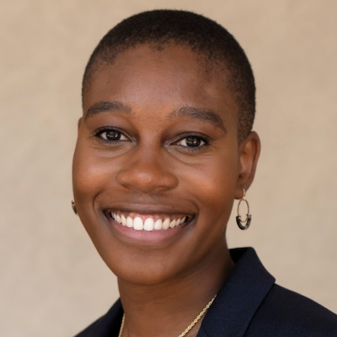 Headshot of Kaela Joibois, MPH, in a white blouse with black collar, dark blue blazer, gold necklace, and gold hoop earrings