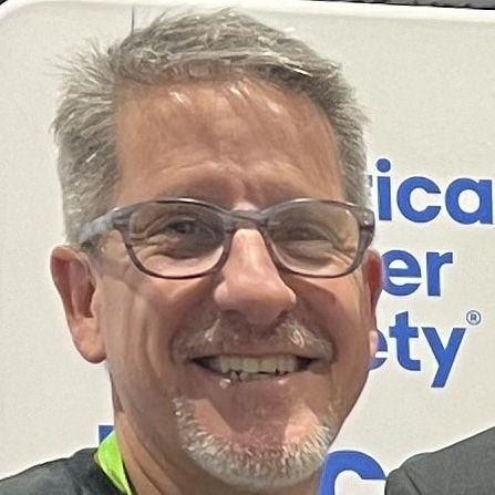 Headshot of Doug Hurst, PhD, standing in front of an American Cancer Society sign