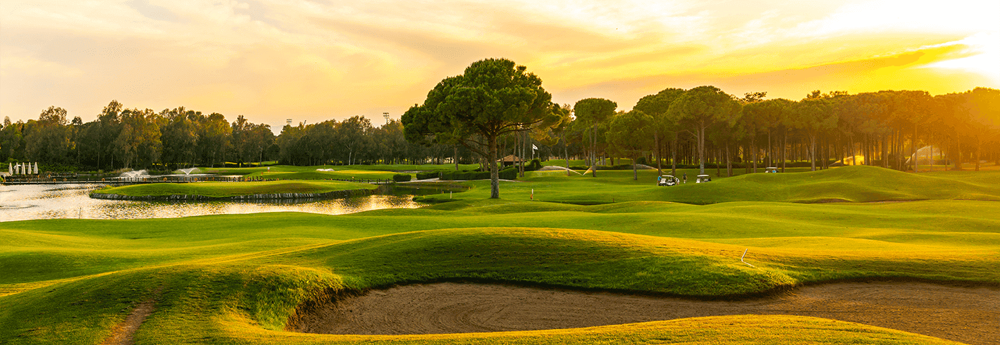 A scenic golf course with green fairways, sand bunkers, and a water feature at sunset