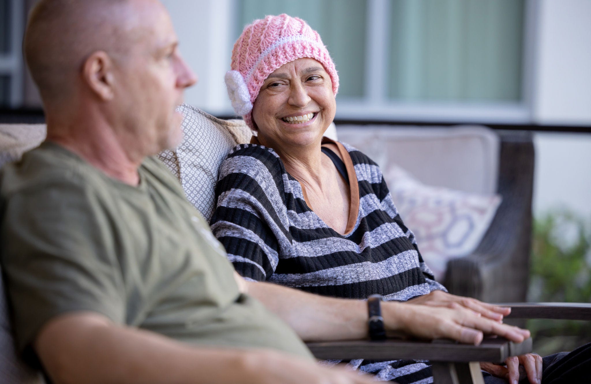 A woman wearing a pink knit hat smiles while sitting and talking with a man.