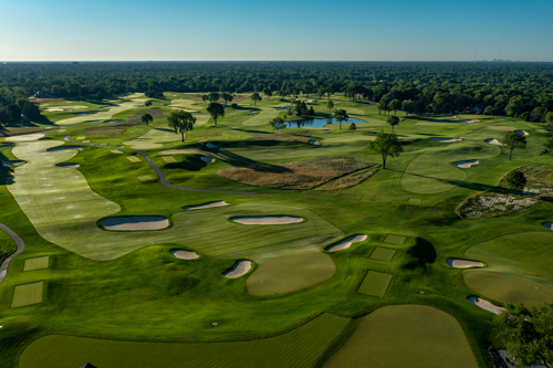 Aerial view of a lush, expansive golf course with multiple fairways, greens, and water features under a clear blue sky