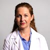 A woman wearing a white lab coat and light blue shirt smiles at the camera