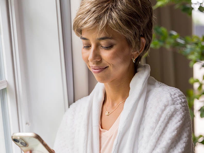 A woman in a relaxed robe looks at her phone, absorbed in what she’s reading or viewing.