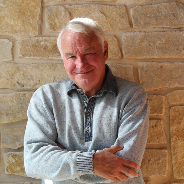 Smiling older man in gray sweater against a stone wall