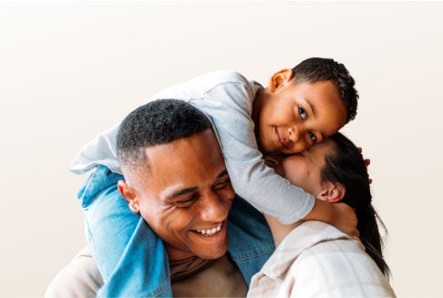 A young boy sits on his fathers shoulders while giving his mother a hug