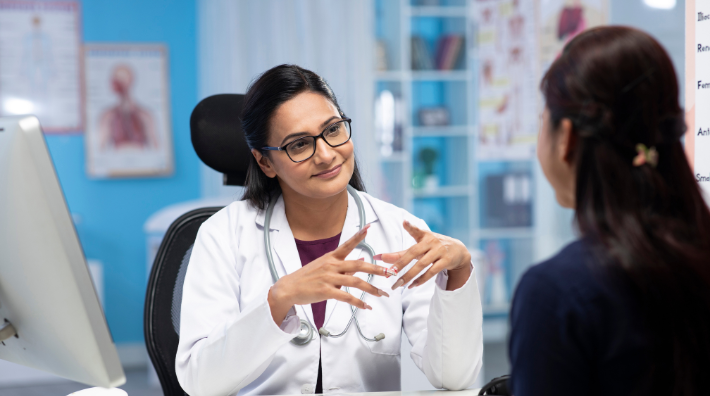 A female doctor behind a desk talks to a female patient