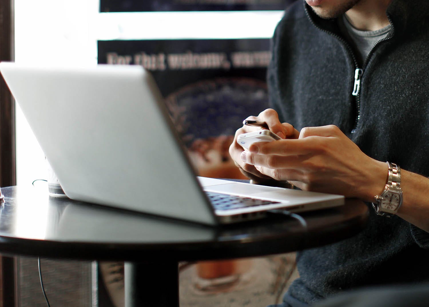 A person using a smartphone while sitting in front of a laptop