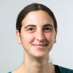 Headshot of Rebecca Landy, PhD, in a green sweater over a black t-shirt, in front of a gray background