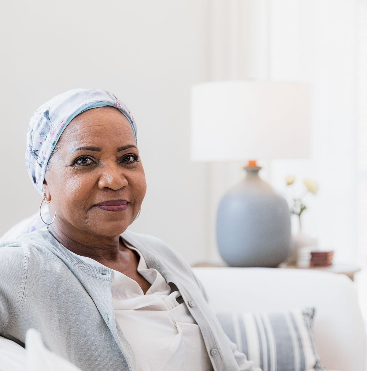 An older woman with a headscarf smiles while sitting in a living room