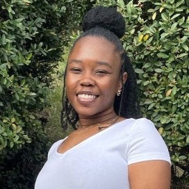 black woman with large bun on top of head wearing white short sleeved shirt in front of trees