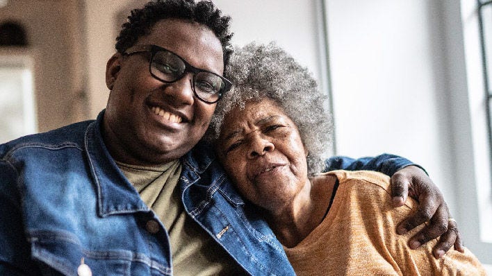 black man wearing glasses with arm around the shoulders of a senior black woman