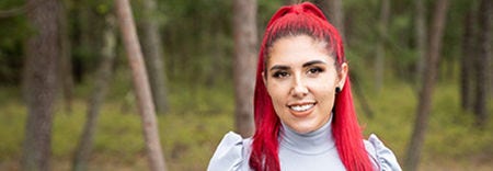 A woman with vibrant red hair wearing a blue shirt, smiling confidently against a neutral background