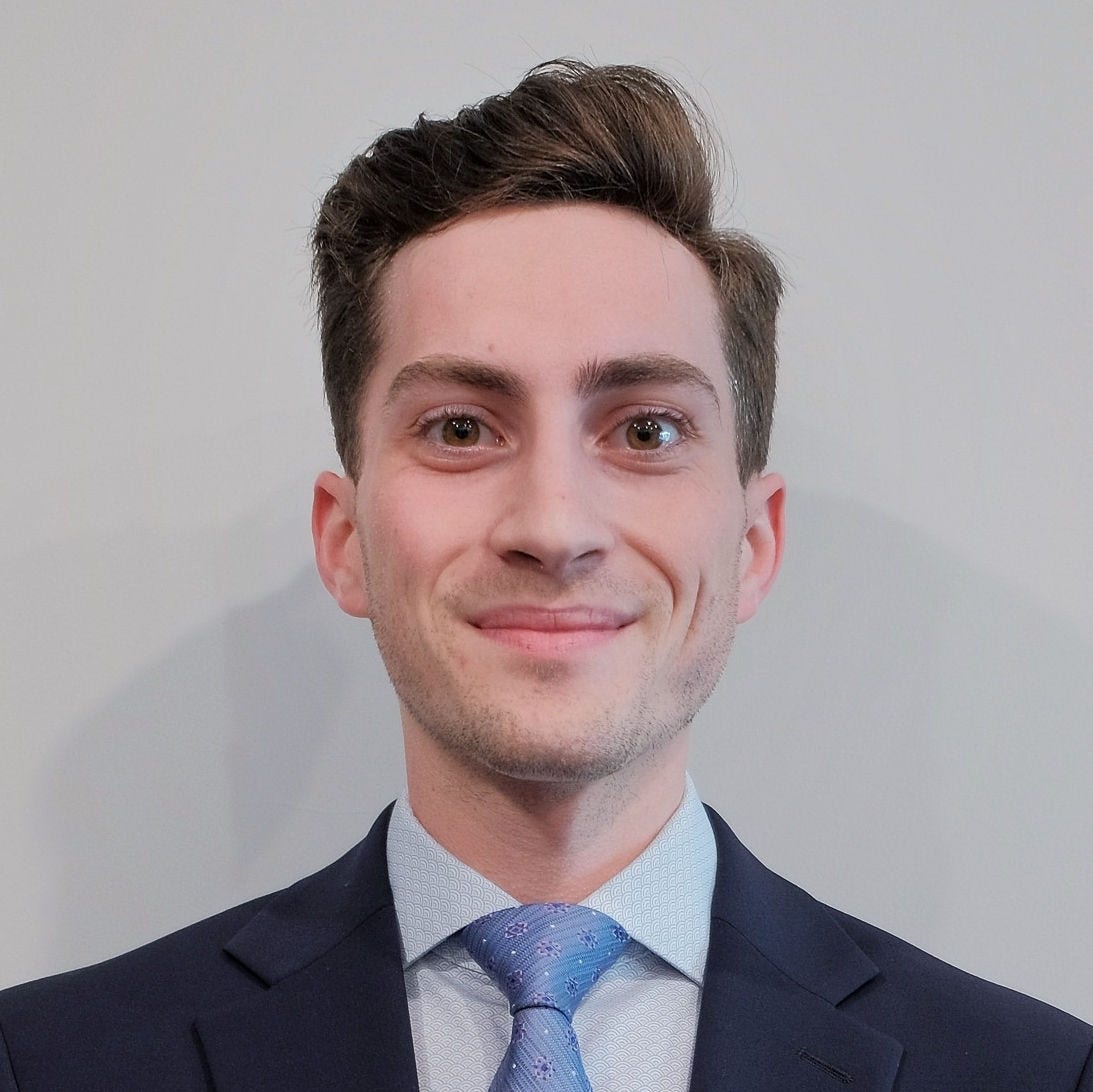 Headshot of Kieran Kelly, MPH, in a dark blue blazer, light blue shirt, and blue tie with red dots