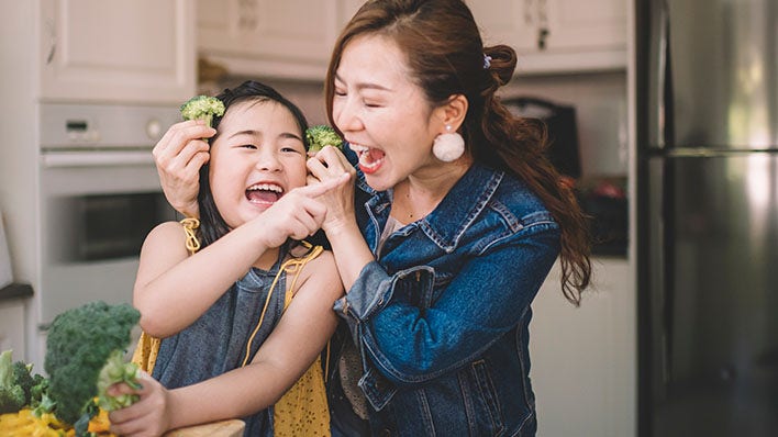 A woman and a young girl enjoying a healthy meal of broccoli together.