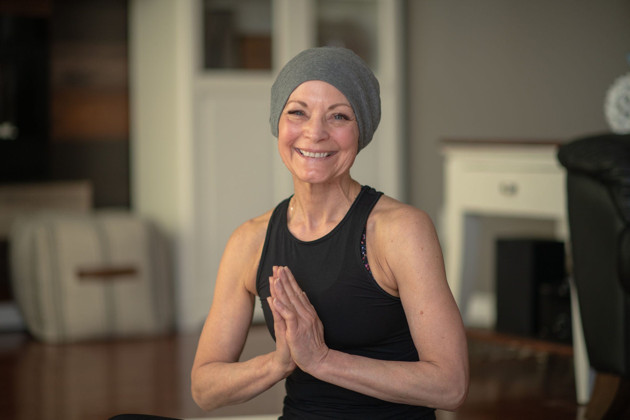 A senior woman with cancer does yoga at home in her living room. She is wearing black active wear.