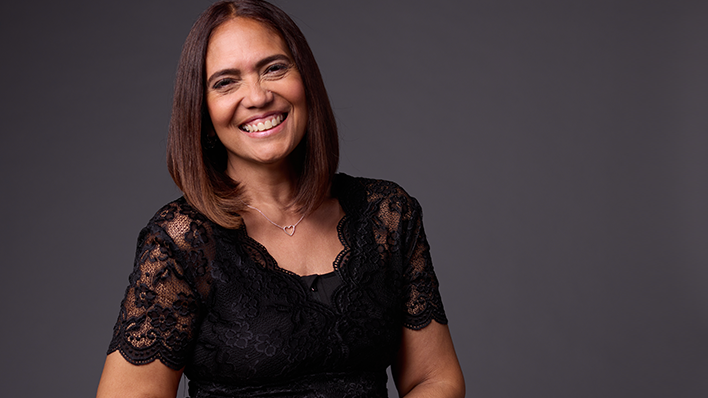 A woman wearing a black lace dress standing against a textured background