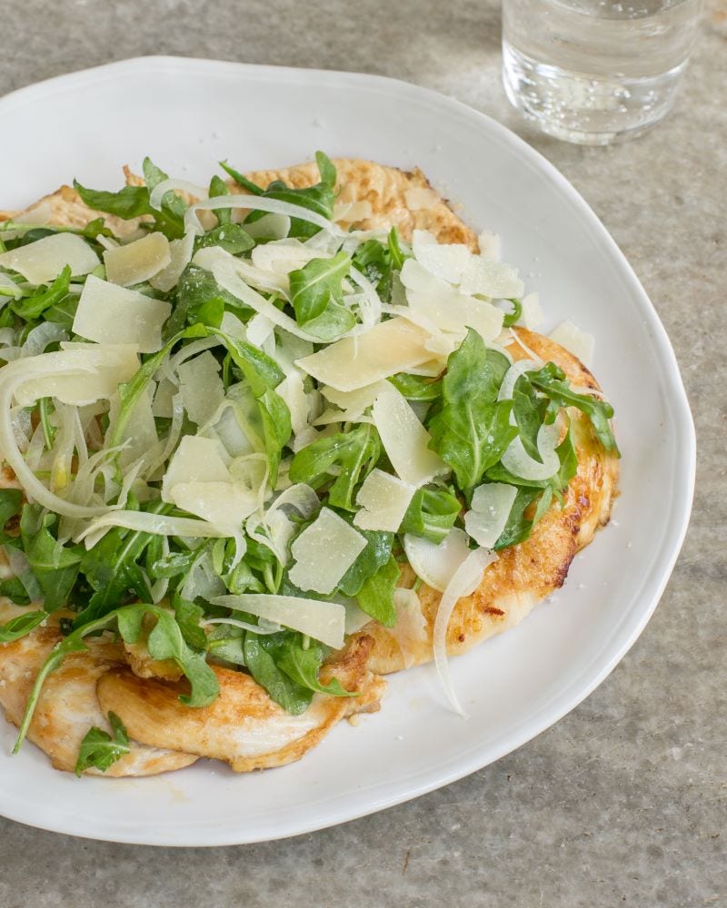 Plate with chicken paillard on a bed of arugula, topped with Parmesan and fennel