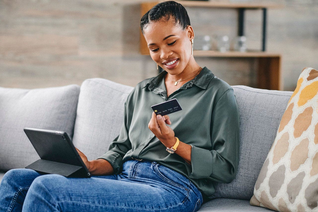 a black woman using a credit card and a tablet while sitting on a couch