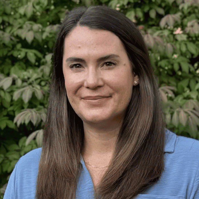 A white woman with long brown hair smiling outdoors