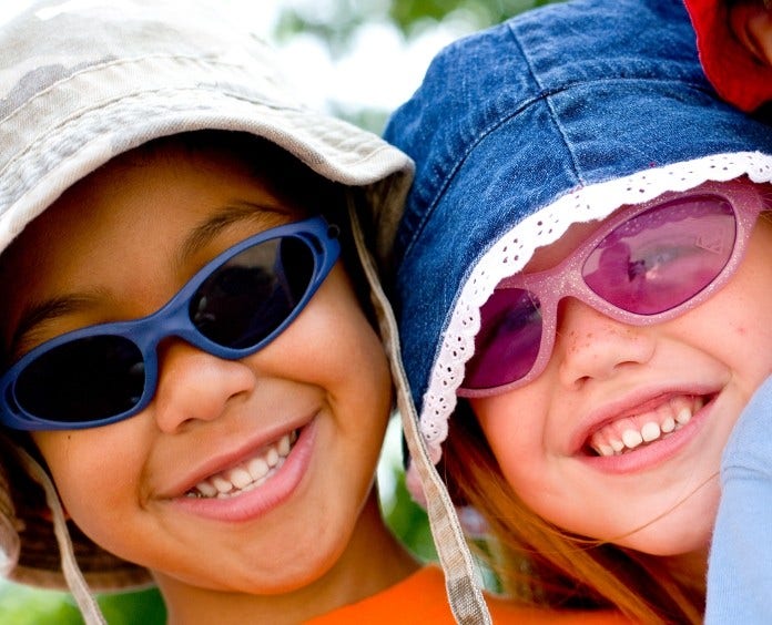 two smiling children wearing sun hats and sunglasses outside