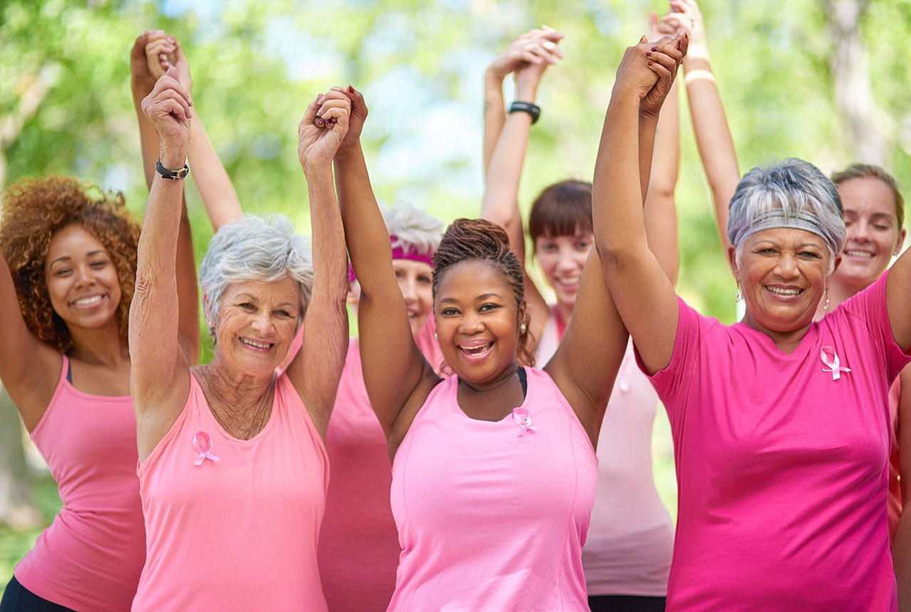 A diverse group of women in pink clothing holding hands and smiling in support of breast cancer awareness