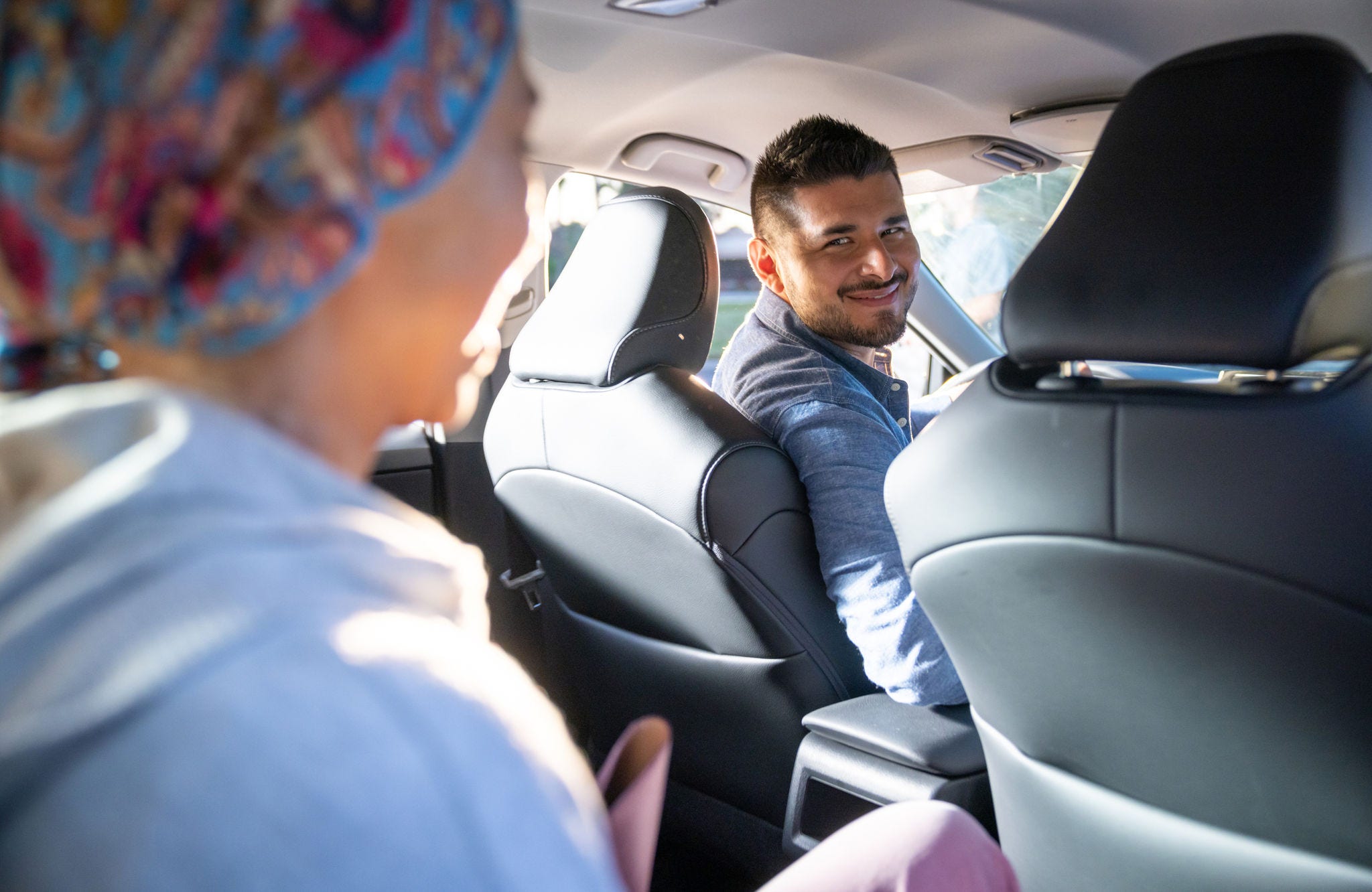 A smiling male driver looks back at a passenger inside a car