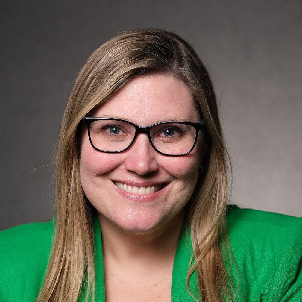 Headshot of researcher Joanne Elena, PhD, MPH, black rimmed eyeglasses, long, blonde hair, bright green blazer over a bright green blouse