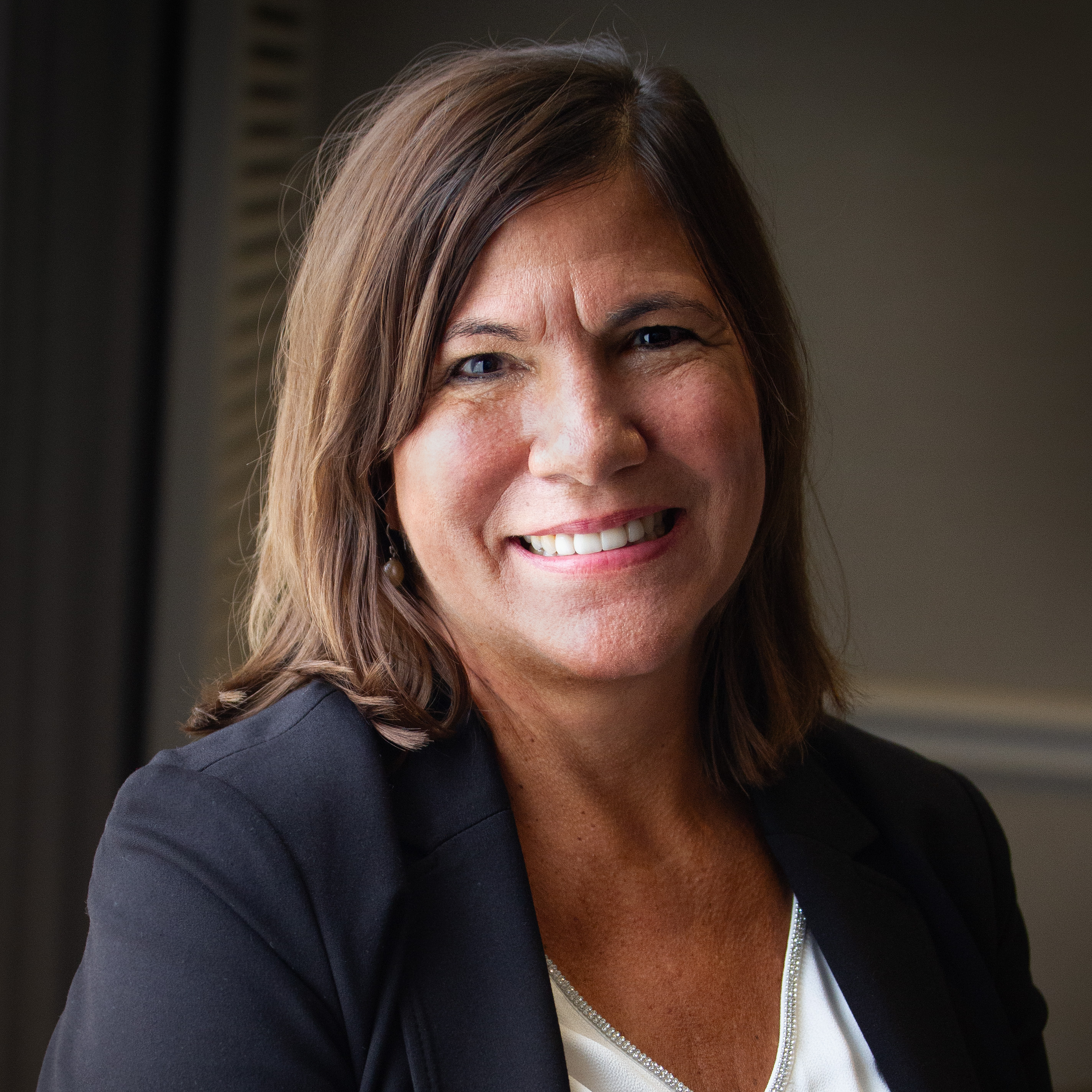 Professional headshot of a smiling woman with shoulder-length brown hair wearing a black blazer