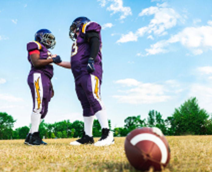 Two youth football players high fiving, footbal on the ground in the foreground. 