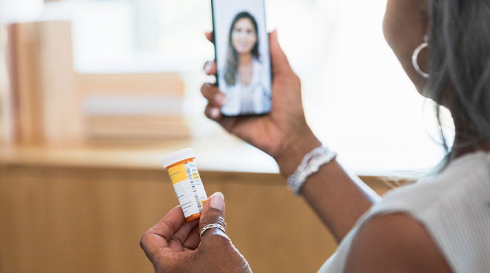 A woman holds her phone up to video chat with one hand and holds a pill bottle in the other hand. 