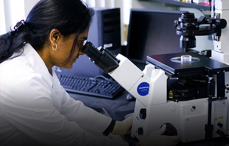 researcher in lab coat looking through a mircoscope