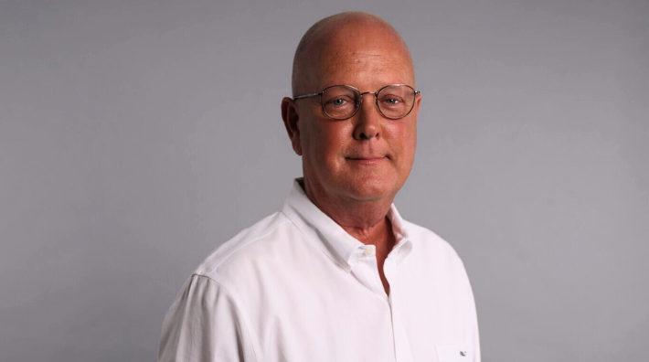 Coach Kevin Kelly, who used his game-time mindset to battle leukemia and became a fundraising organizer and an advocate for cancer research, stands in front of a gray background