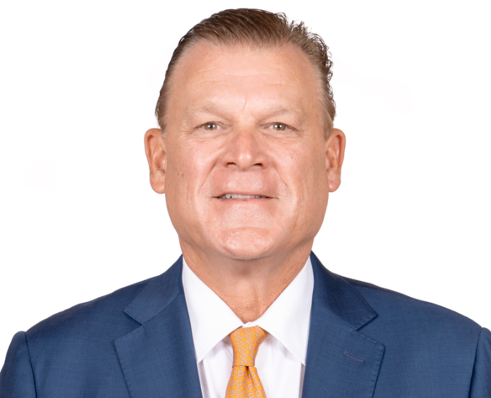 A man in a blue suit and orange tie smiling in a professional headshot