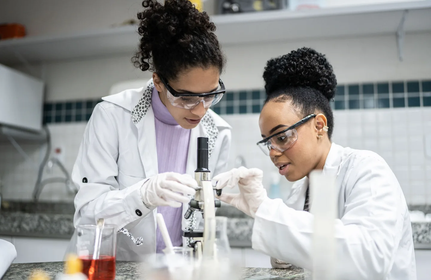 Two scientists in a lab examining a sample through a microscope