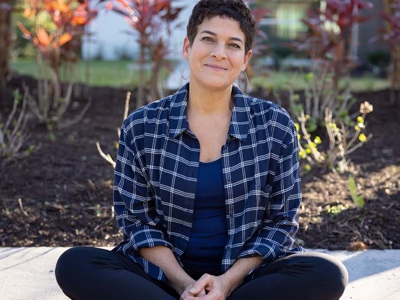 A woman sits with her legs crossed outside on the sidewalk