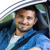 Hombre sonriente sentado en un auto, usando el cinturón de seguridad