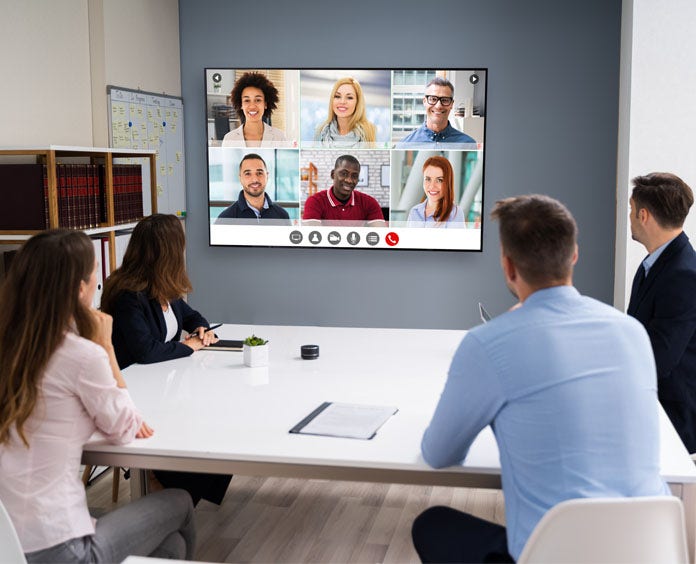 A team of professionals in a meeting room, focused on a video conference displayed on a big screen in front of them.