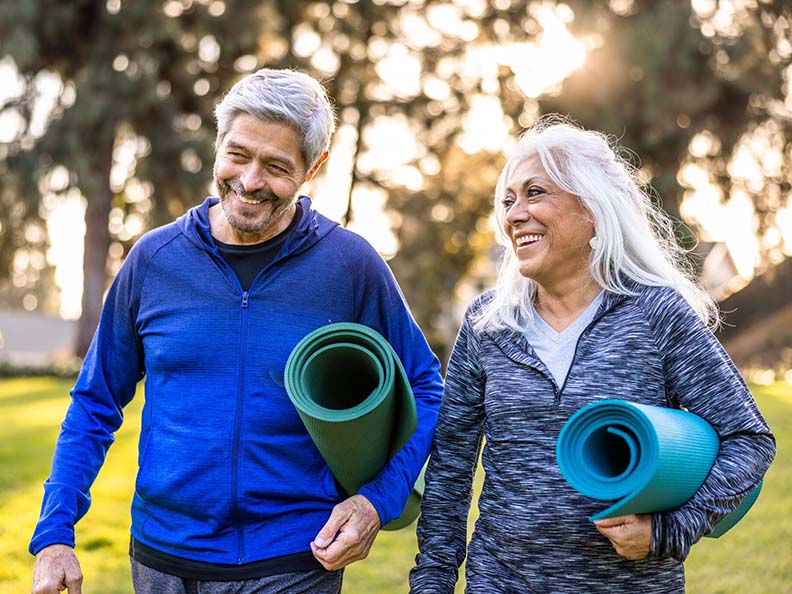 Senior couple holding yoga matts walking outside 