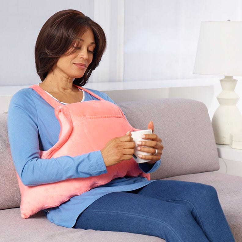 A woman on a couch holds a cup, wearing mastectomy pillow living space.