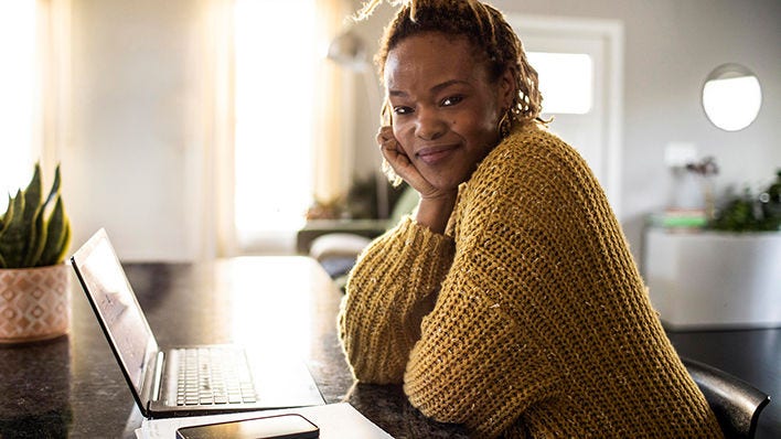 Mujer sonriente sentada en una mesa con una laptop y un teléfono.