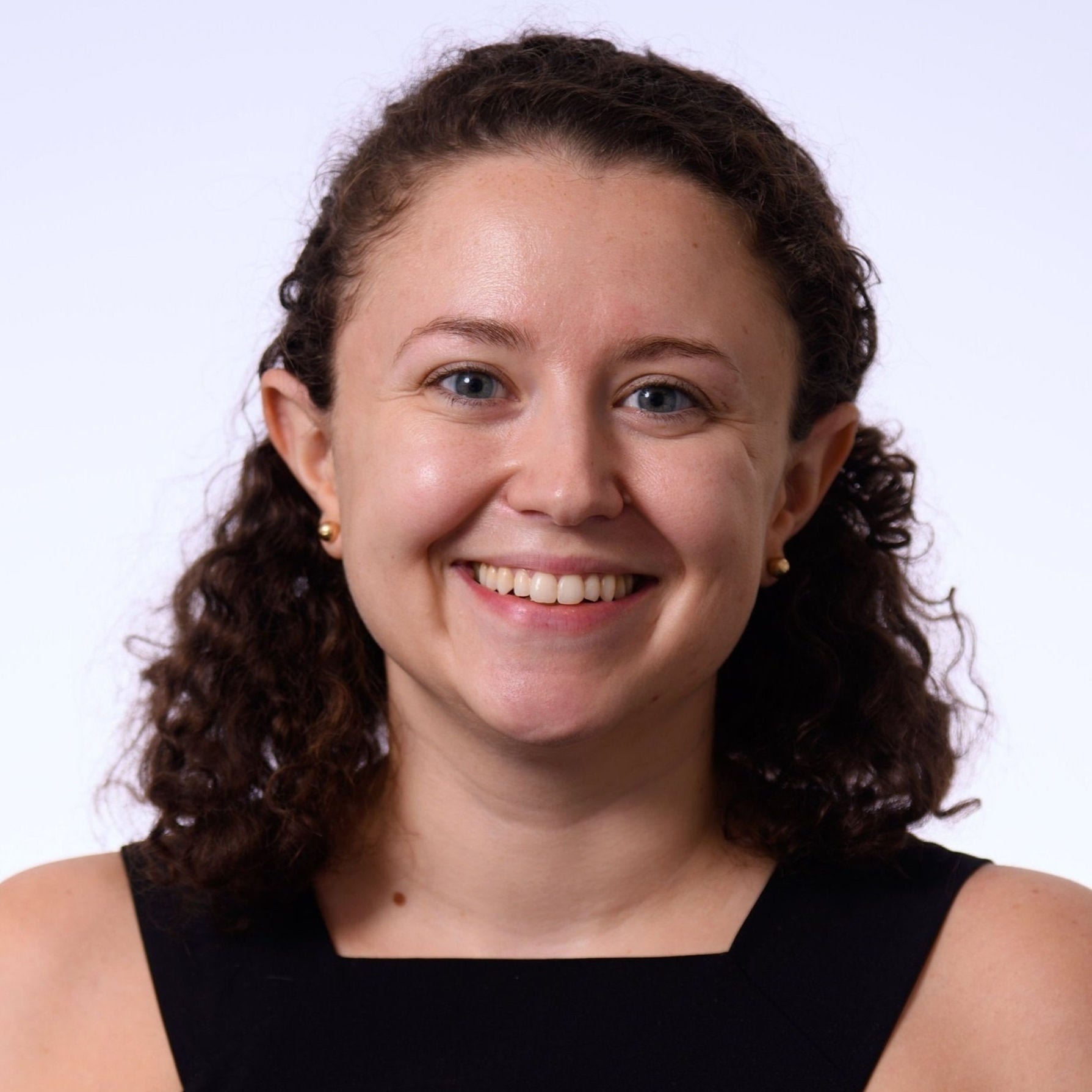 Woman with curly hair behind ears, gold bead earrings and square neck dress with bare shoulders