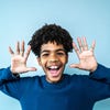  A young boy joyfully raises his hands in the air, smiling brightly.