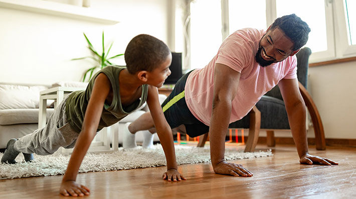 A boy and a man do pushups in a living room with a white rug and white couch. 